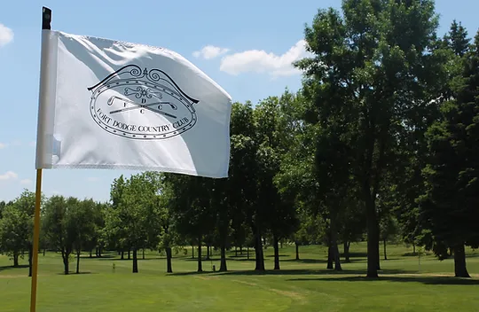 A white flag bearing the Country Club logo flights in front of a well-manicured golf green and stand of trees.