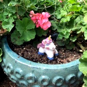 A flower pot with a sculpted clay unicorn in it.