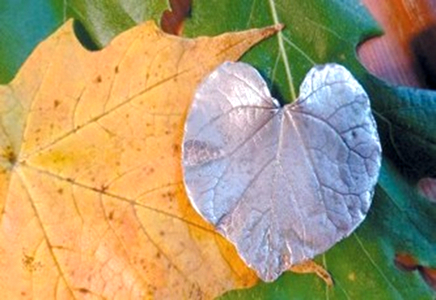A leaf-shaped silver metal clay pendant on top of colorful fall leaves.
